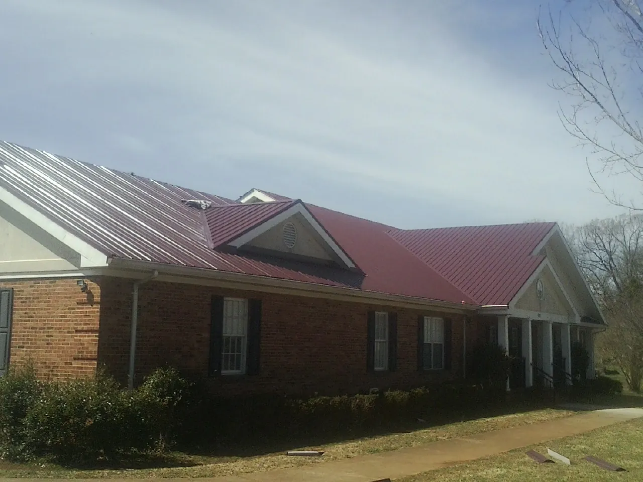 Red metal roof with gabled entries on a long brick building, from a Hail Damage Roof Repair job in Oakdale