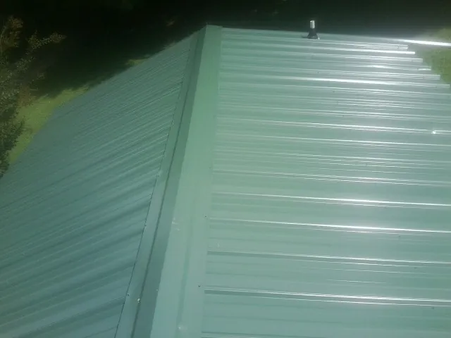 New green metal panels meeting at the ridge of a roof — Flat Roof Repair work by our crew in Oakdale