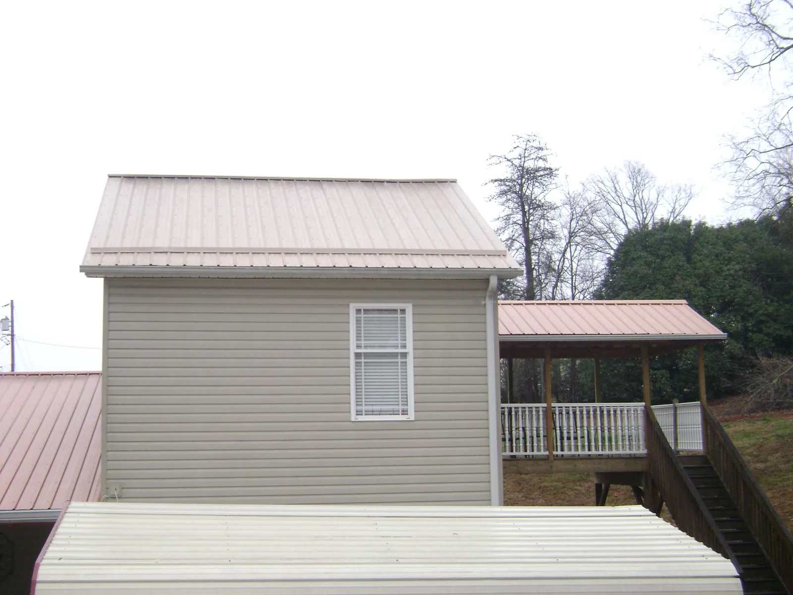 Tan metal roofs on a two story addition and attached porch, from a Roof Replacement job in Oakdale